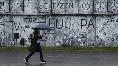En mur med väggmålningar med EU-tema i rumänska staden Sibiu. I förgrunden en förbipasserande  invånare med ett paraply i handen. 