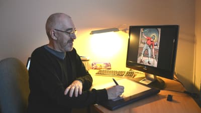 Äldre man sitter framför dator. Han håller i en penna och ritar på en ritplatta. På datorskärmen synns en frägglad teckning av en människa.