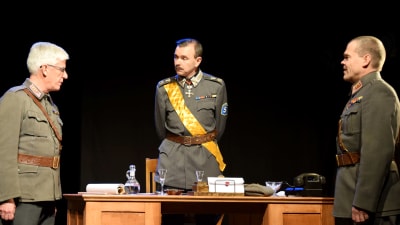 Scen ur teatern Mannerheim - mannen och myten. Mannerheim (Stefan Elf) står vid ett skrivbord. Till vänster syns skådespelaren Mats Enberg och till höger skådespelaren Kari Danielsson.