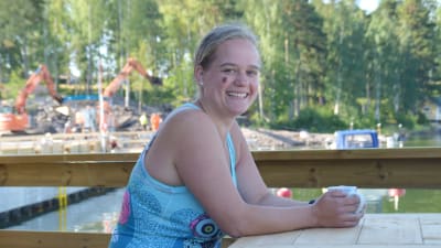Ragna-Lise Karlsson sitter med en kaffekopp i händerna vid en uteservering. I bakgrunden skymtar en småbåtshamn.