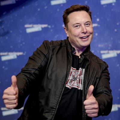 Elon Musk poserar på röda mattan. Han ler och håller tummarna upp.