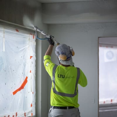 Rakennusmies työssään Skanskan kerrostalokohteessa tasoittamassa seiniä ja kattoa ruiskutasoitteella, Munkkiniemi, 25.1.2019.