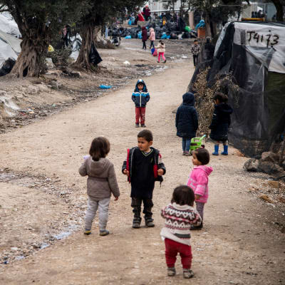 Några barn står i en grupp på ett flyktingläger i Grekland.