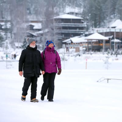 Mies ja nainen kävelemässä Hotel & Spa Resort Järvisydämen ulkoilureitillä, hotellin vastaanotto taustalla.