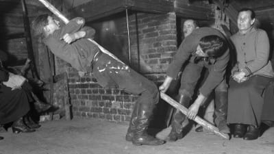 En man leker leken "stiga upp med stången". Bilden är tagen 1935 i Bromarf, Rilaks.