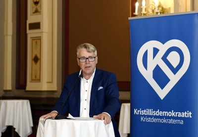 Peter Östman står och talar i en mikrofon bredvid Kristdemokraternas banderoll.