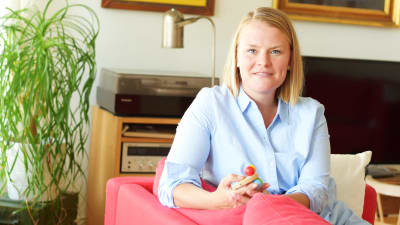 Lena Sommer sitter i en röd soffa och har en barnleksak i handen.