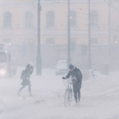 Pyöräilijä taluttaa pyörää lumimyräkässä Senaatintorin vieressä Helsingissä.