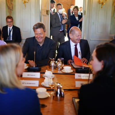 Sanna Marin och Magdalena Andersson, med ryggen mot kameran, träffar Tysklands regering vid ett långbord där kaffe är framdukat.