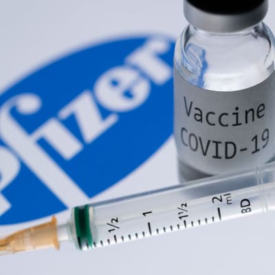 Bilden visar Pfizer-logon, en glasburk med covid-19-vaccin och en spruta.