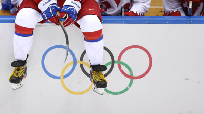 Ishockeyspelare sitter på sargen framför de olympiska ringarna.