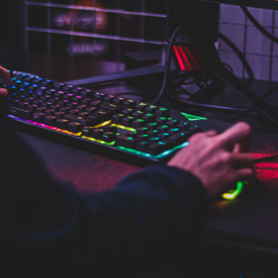 En pojke sitter i ett mörkt rum vid en dator med neonlysande tangentbord och mus.