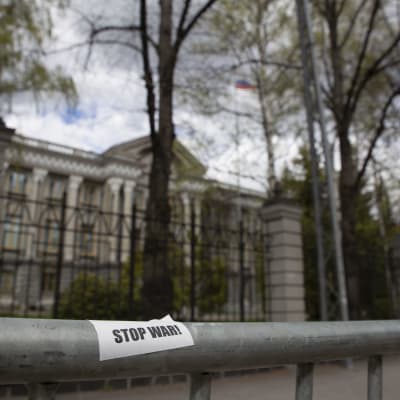 På ett metallstaket framför Rysslands ambassad, en stor klassisk byggnad omgiven av träd, finns ett klistermärke med texten Stop War.