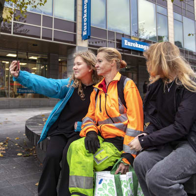 Tyttö ottaa selfietä kahden muun henkilön kanssa ulkona. 