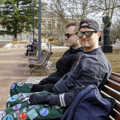 Eetu Hakala istuu ystävänsä kanssa puiston penkillä. Heillä on päällään opiskelijahaalarit.