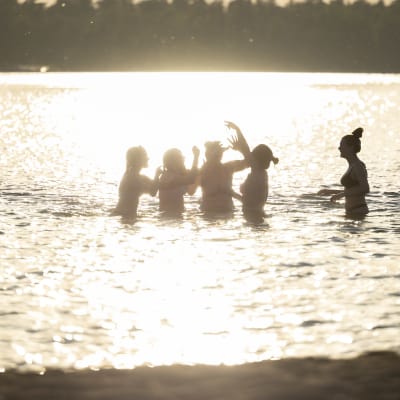 Nuoria naisia uimassa. Aurinko loistaa veteen.