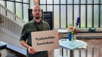 En man håller i en skylt där det står "Pysäytetään luontokato" (översättning: "Låt oss stoppa förlusten av biologisk mångfald")
