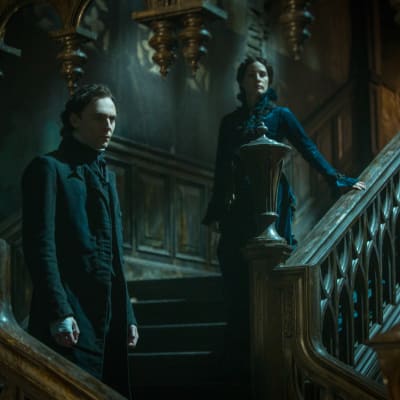 Tom Hiddleston och Jessica Chastain står i bred trappa i skräckens boning.