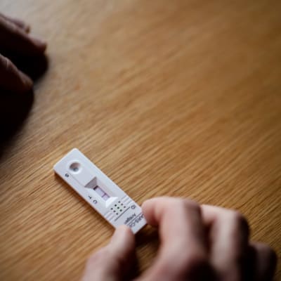 Henkilö tekee koronapikatestiä ruokapöydän ääressä.
