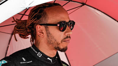 Lewis Hamilton står under ett paraply.