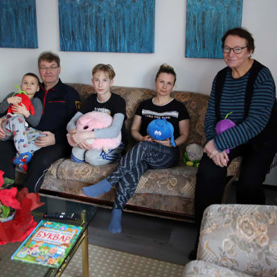 Raija ja Kari Jääskeläinen sekä Tetjana Vinitska lapsiensa, Maksymin ja Daniilin, kanssa olohuoneen sohvalla.