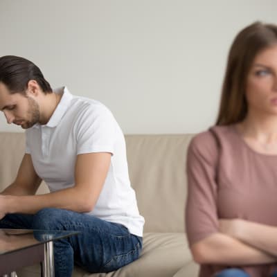 Man och kvinna sitter vända från varandra på soffa