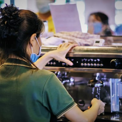 En kvinna står med ryggen mot kameran och lagar kaffe i ett kafé. 