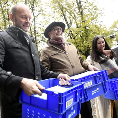 Sampo Terho, Matti Torvinen och Tiina Elovaara håller plastlådor med Blå framtids anhängarkort.