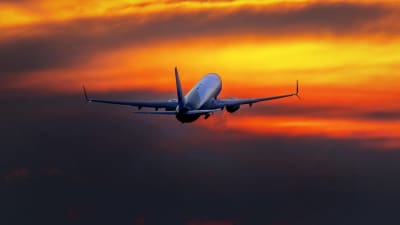 Flygplan lyfter, morgonrodnad i bakgrunden.