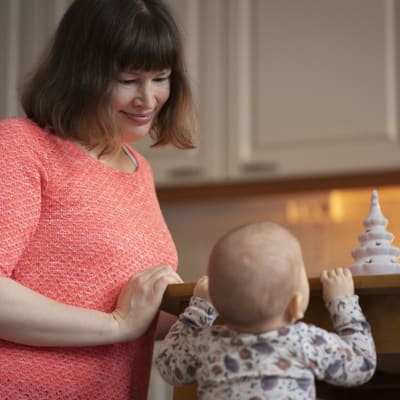 Eevaliisa Korvonen katsoo hymyillen hänen vauvaansa, joka ottaa tukea keittiön pöydästä.