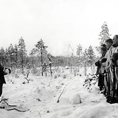 Soldater under vinterkriget står uppställda på led med huvudbonaderna i händerna.