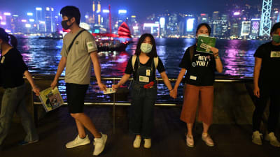 Unga demonstrerar i Hongkong, i bakgrunden ses vatten och Hongkong ljus. 