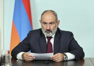 Armeniens premiärminister Nikol Pasjinjan sitter vid ett bord med Armeniens flagga bakom sig. Han håller ett tv-sänt tal och ser allvarlig ut.