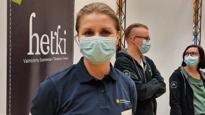 En kvinna med munskydd som står framför en mässmonter. 
