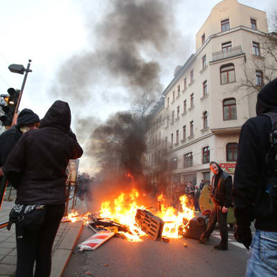 Vänsteranhängare står vid en brinnande barrikad efter våldsam motprotest mot nynazistisk demonstration.