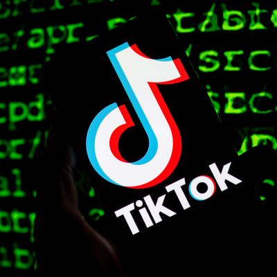 Tik Tok yhtiön logo puhelimen ruudulla. Taustalla näkyy lähdekoodia.