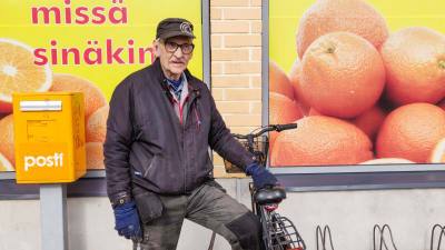 En äldre man håller i en cykel. Han står utanför en mataffär.