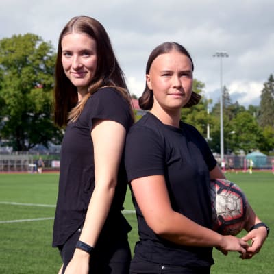 Felicia Gröning och Jill Illman står på en konstgräsplan och håller i en fotboll.