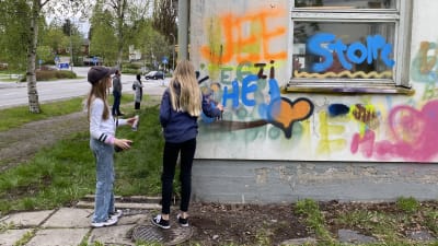 Två unga tjejer målar grafitti på skolbyggnad.