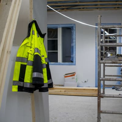 En färggrann arbetsjacka hänger på en spik på ett bygge.