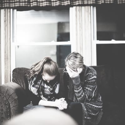 Två kvinnor sitter i en soffa och håller huvudet i händerna
