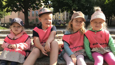 Fyra dagisbarn sitter ute på en trappa.
