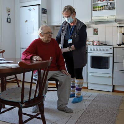 Eläkkeeltä töihin kutsuttu lähihoitaja Seija Kakko keskustelee kotihoidon asiakas Aarne Jantusen kanssa Jantusen keittiössä.
