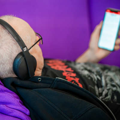 Henkilö makaa sohvalla ja kuuntelee kuulokkeet päässä kännykkä kädessään äänikirjaa.