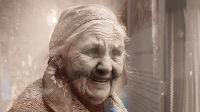 En äldre leende kvinna med huckle på huvudet.
