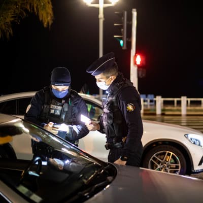 Franska poliser står vid en bil i mörkret, de kollar förarens dokument.