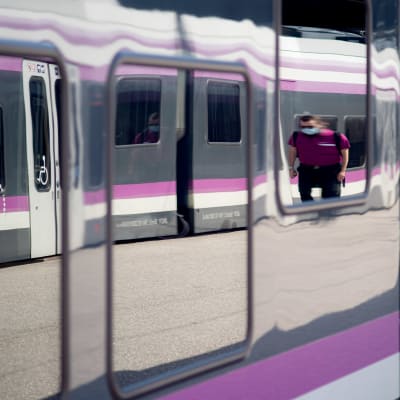 Junan ikkunasta heijastuu, kun HSL:n henkilökunnan jäsen kävelee laiturilla. 
