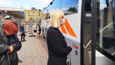 Kvinna bär vitt ansiktsskydd vid en buss med öppen dörr.