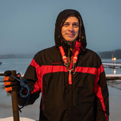 En man i vindtygsjacka med luvan uppdragen, håller i en käpp och har isdubbar runt halsen