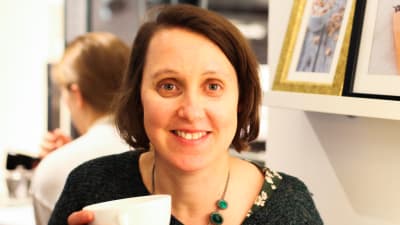 En person (Annika Sandelin) håller i en kaffekopp och ler.
